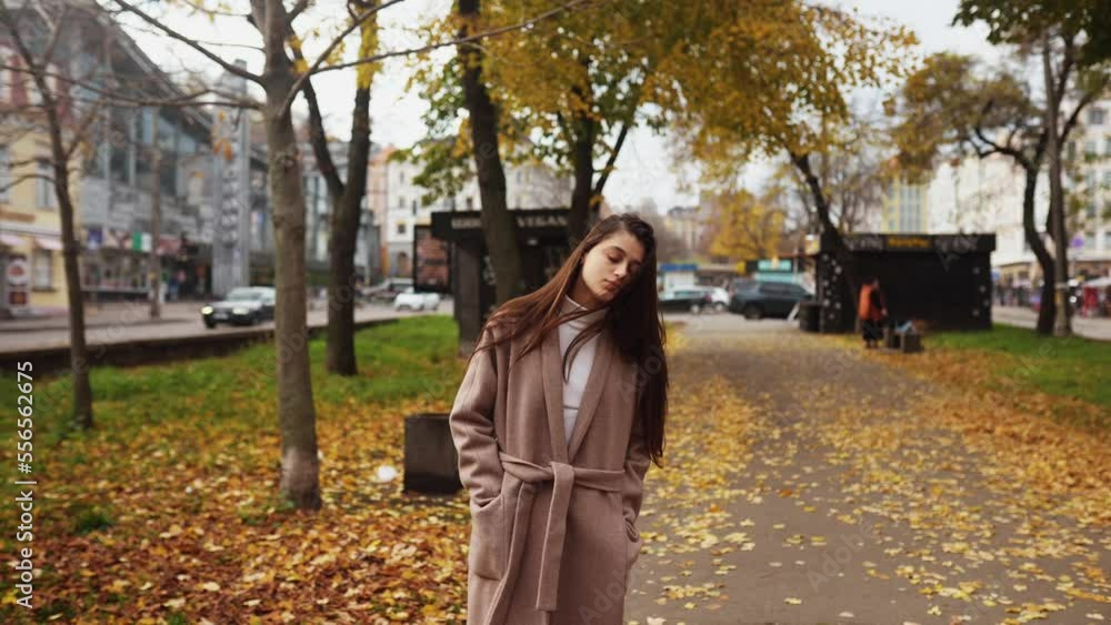 Young woman in an autumn coat walks along an alley Young woman in an autumn coat walks along an alley