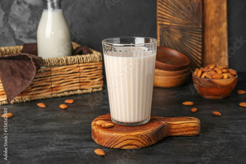 Wooden board with glass of almond milk on dark background photo