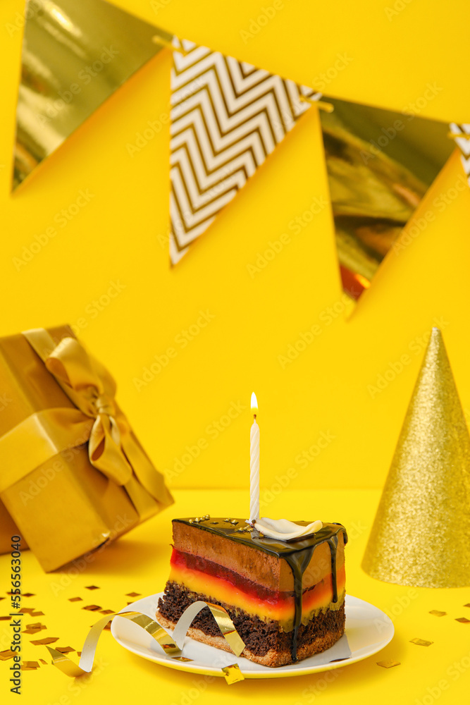 Birthday cake, party hat, gift, flags and confetti on yellow background