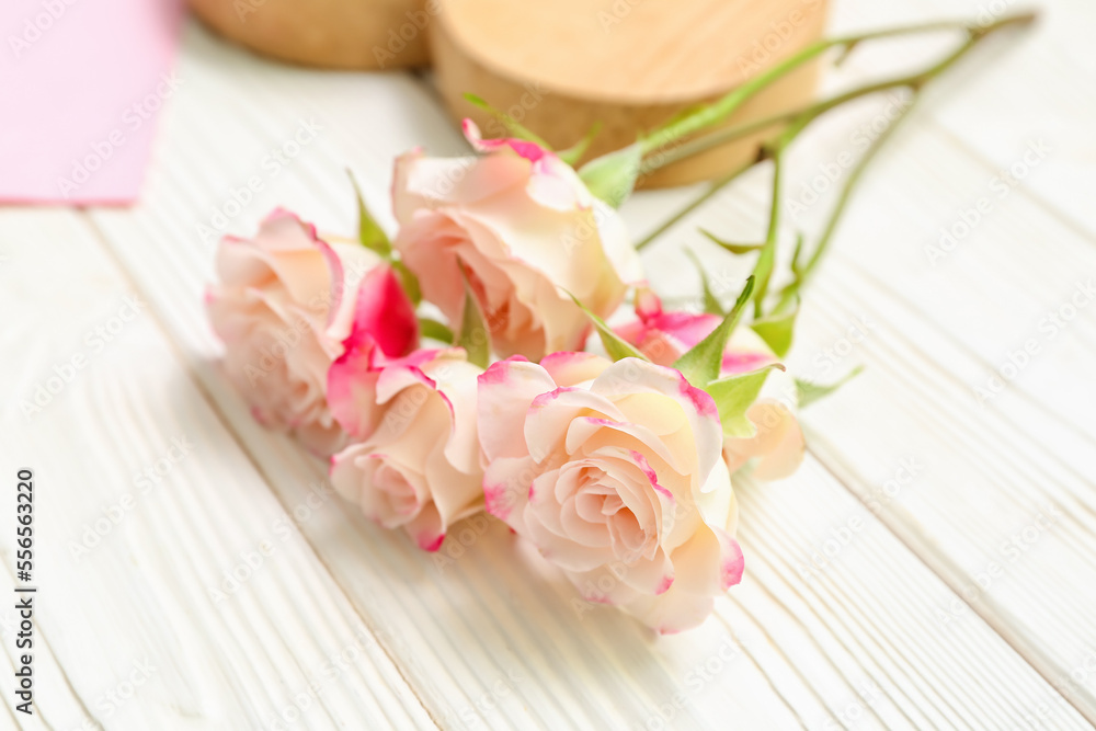 Branch of beautiful rose flowers on light wooden background, closeup
