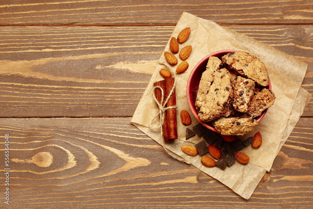 Bowl with tasty biscotti cookies, almond nuts, cinnamon and chocolate on wooden background Bowl with tasty biscotti cookies, almond nuts, cinnamon and chocolate on wooden background