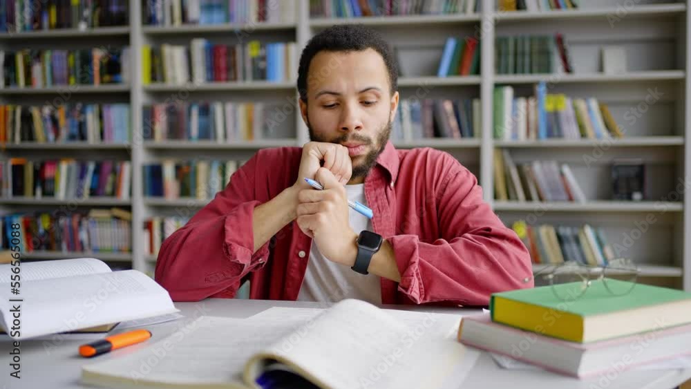 Multi-ethnic man student surrounded by books and literature, working on assignment in library campus Multi-ethnic man student surrounded by books and literature, working on assignment in library campus