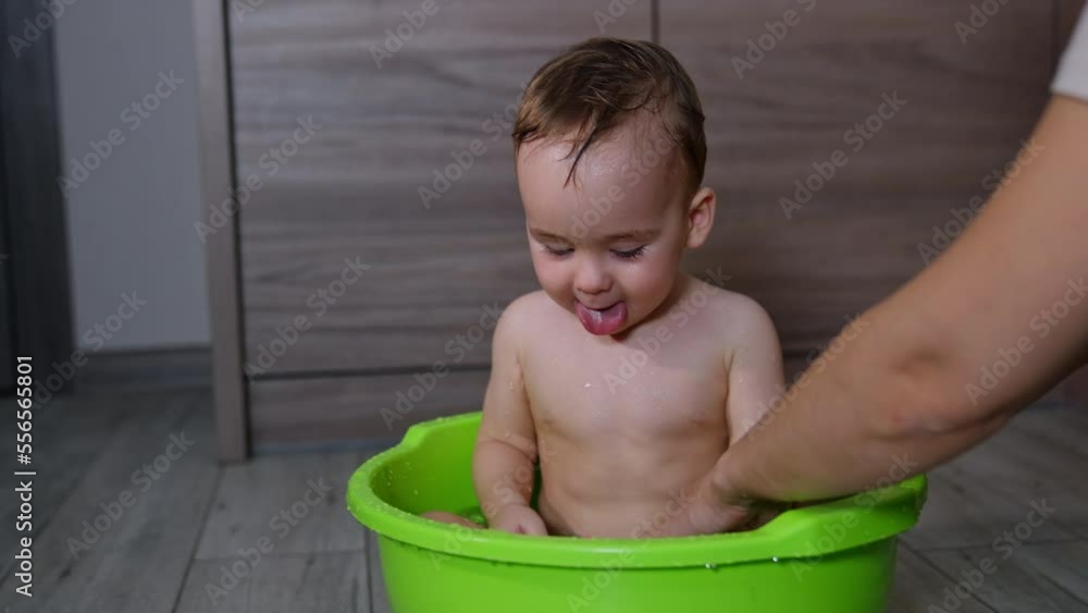 Caring mom washing her lovely baby sitting in the washbowl. Calm boy plays with rubber toy and pulls it into mouth. Caring mom washing her lovely baby sitting in the washbowl. Calm boy plays with rubber toy and pulls it into mouth.