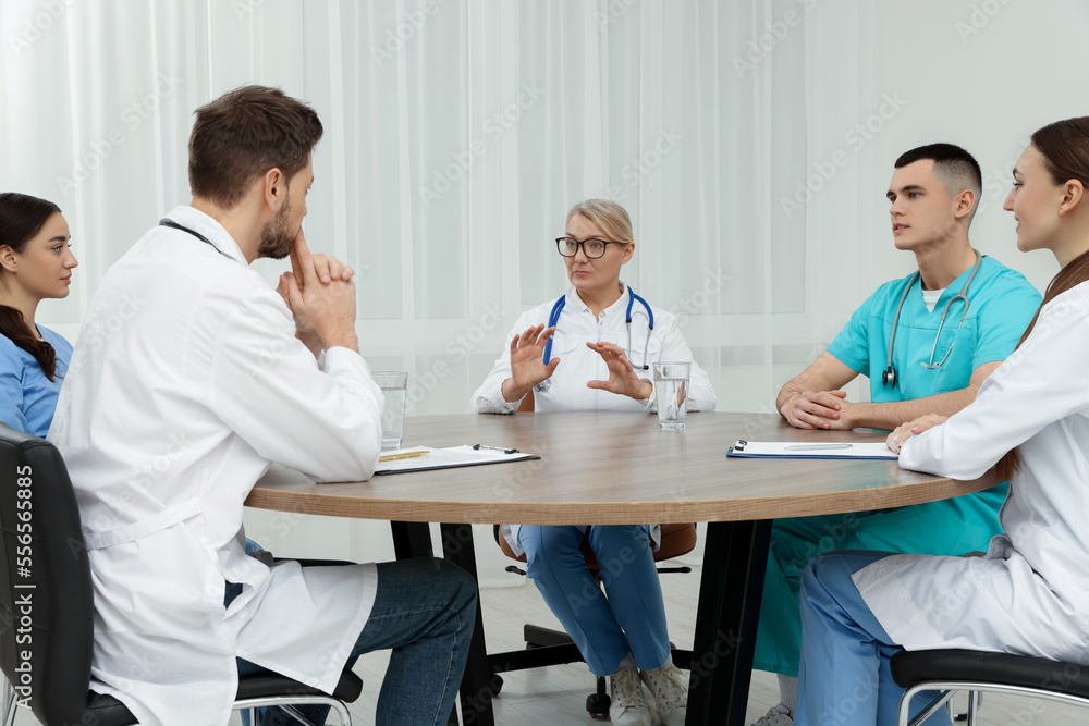 Medical conference. Team of doctors having discussion at wooden table in clinic Medical conference. Team of doctors having discussion at wooden table in clinic
