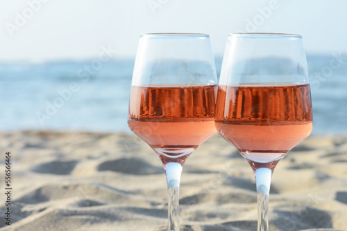 Glasses of tasty rose wine on sand near sea, closeup. Space for text