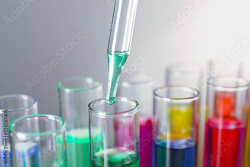 Dripping liquid from pipette into test tube on grey background, closeup