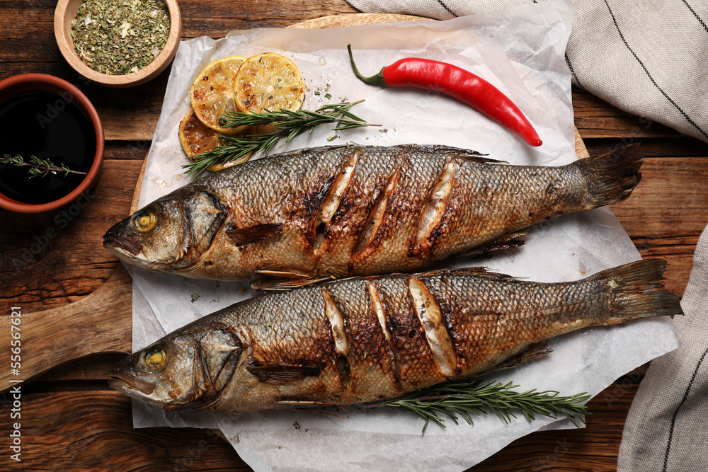 Delicious baked sea bass fish and ingredients on wooden table, flat lay Delicious baked sea bass fish and ingredients on wooden table, flat lay