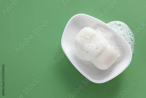 Dish with soap bar and fluffy foam on green background, top view. Space for text