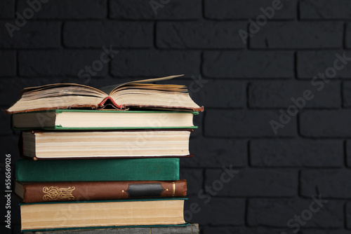 Stack of old hardcover books near black brick wall, space for text