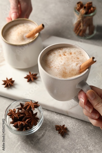 Women holding glass cups of delicious eggnog with cinnamon and anise at light grey table, closeup