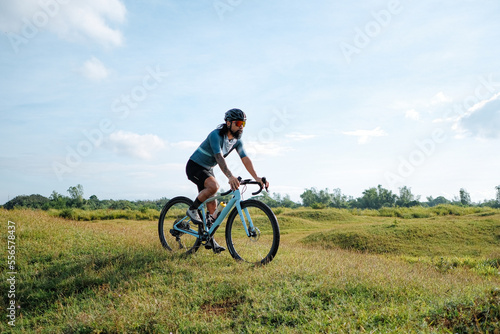 A young bearded cyclist is biking through a field