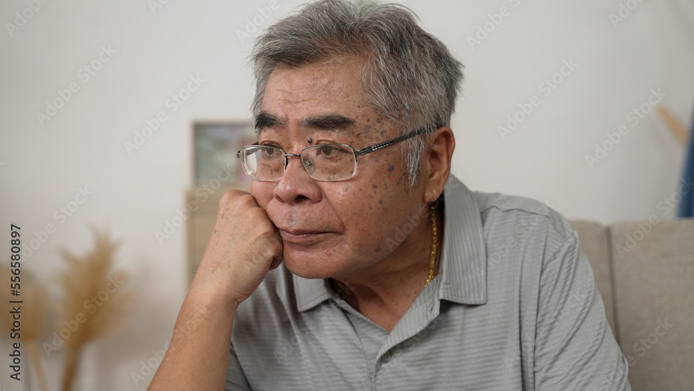 old age people and problem concept. senior Korean man in glasses thinking on sofa at home alone during virus outbreak. older korean male wearing gold chain and feel confused with hand on chin rest old age people and problem concept. senior Korean man in glasses thinking on sofa at home alone during virus outbreak. older korean male wearing gold chain and feel confused with hand on chin rest