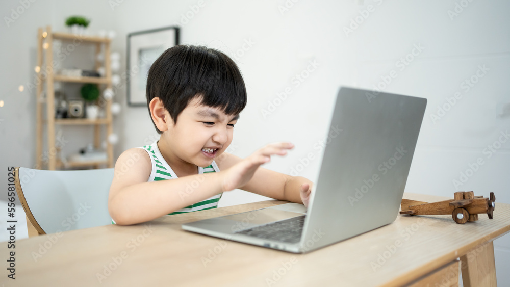 Asian young Little boy addicted playing video game on laptop at home. alone playing tablet computer ipad, he bend down head in his hands, feeling upset, stressful, tired. Digital Addiction. Asian young Little boy addicted playing video game on laptop at home. alone playing tablet computer ipad, he bend down head in his hands, feeling upset, stressful, tired. Digital Addiction.