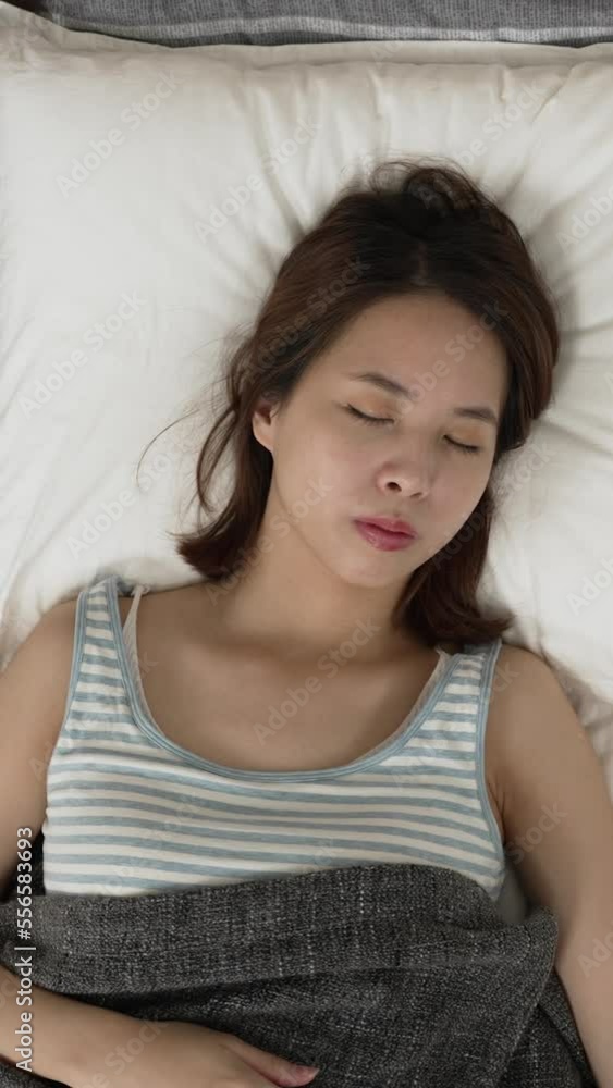 Vertical Screen: Top view from above asian woman lying under blanket in bed. nervous female with frowning face turn over on pillow with nightmare. Vertical Screen: Top view from above asian woman lying under blanket in bed. nervous female with frowning face turn over on pillow with nightmare.
