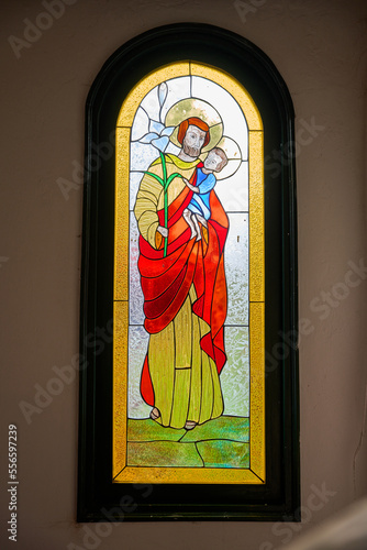 stained glass window of the church with the image of St. Joseph and baby Jesus. religious image of a robed man holding a child in the window of the church. artwork painted on a window of the chapel. 