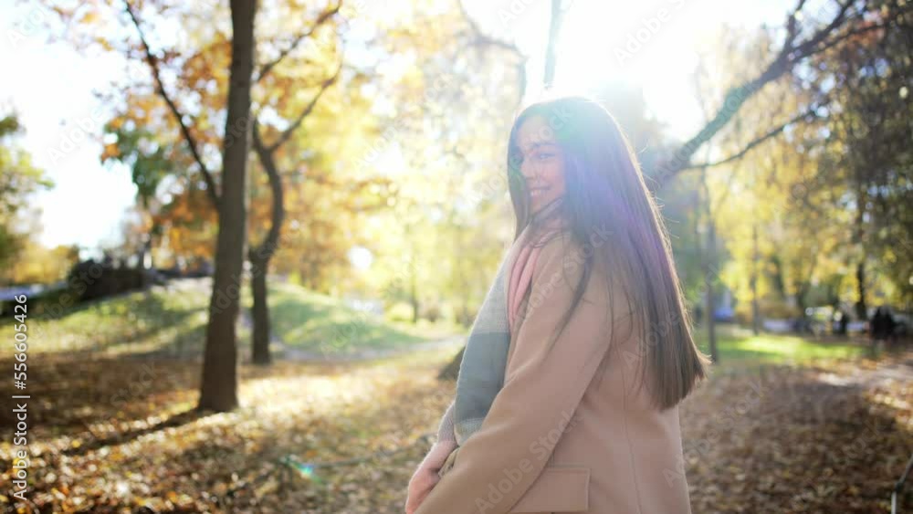 Side view portrait of caucasian beautiful young woman going forward in park with glass of coffee and drinking it. Walk in autumn park against nature landscape with trees and yellow-gold fallen leaves. Side view portrait of caucasian beautiful young woman going forward in park with glass of coffee and drinking it. Walk in autumn park against nature landscape with trees and yellow-gold fallen leaves.
