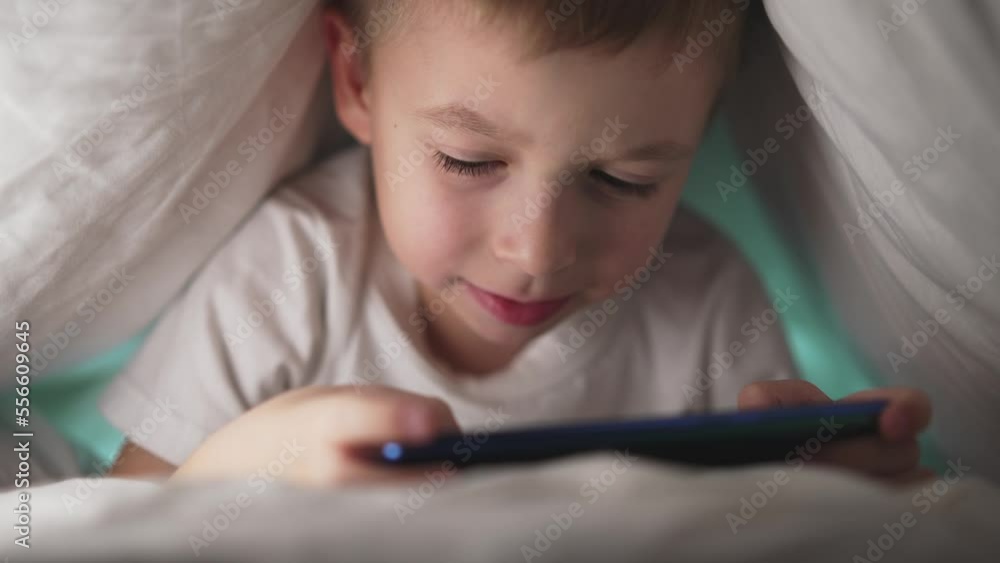 Bottom view of child who wrapped up in blanket and plays mobile phone. Online social networks. Smile and happy. Leisure activity in childhood. Holidays and rest. Baby boy watching and touch at screen. Bottom view of child who wrapped up in blanket and plays mobile phone. Online social networks. Smile and happy. Leisure activity in childhood. Holidays and rest. Baby boy watching and touch at screen.