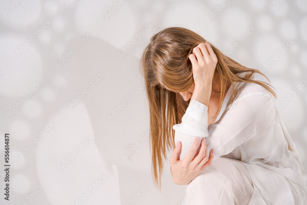 Thoughtful sweet woman posing on light background with light art shadows in a translucent white shirt, sad mood and longing, gesturing with her hands in the studio. Conceptual photo from copy space Thoughtful sweet woman posing on light background with light art shadows in a translucent white shirt, sad mood and longing, gesturing with her hands in the studio. Conceptual photo from copy space