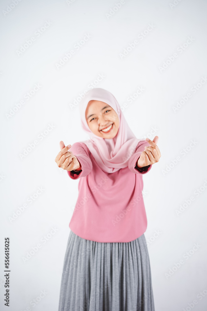 Beautiful Asian woman in pink sweater and hijab showing Korean heart with two fingers crossed, express joy and positivity on white background Beautiful Asian woman in pink sweater and hijab showing Korean heart with two fingers crossed, express joy and positivity on white background