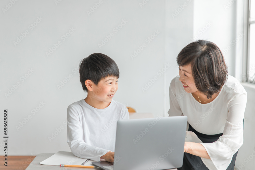 学校の教室でノートパソコンを使いながら勉強する男子小学生と女性講師（教育・先生・授業・家庭教師）
