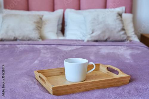A cup of tea on a tray is on the bed. Breakfast in bed.