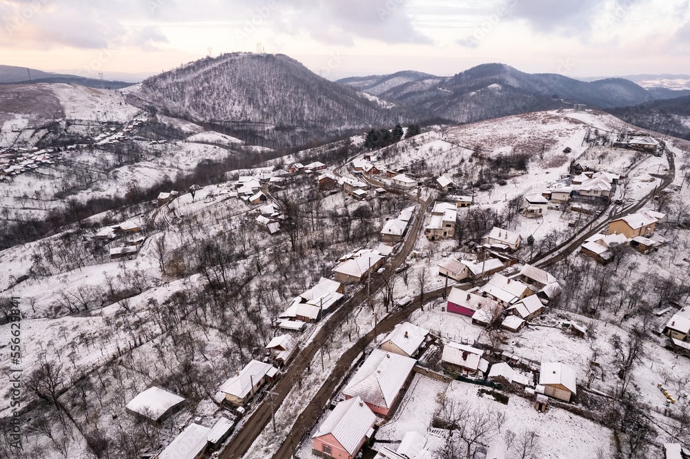 Aerial view of a village covered in snow, in a mountainous rural area, from Romania. Captured with a drone, in winter conditions.
