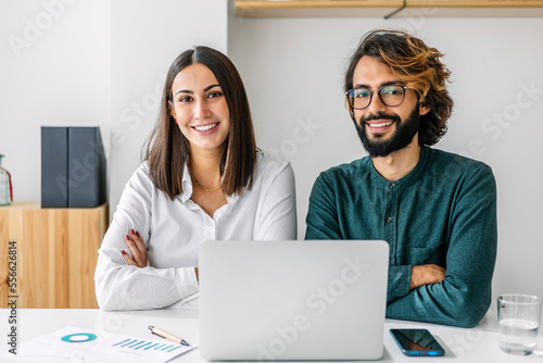 Smiling business colleague with arms crossed at desk in office photo