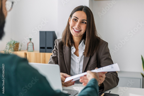 Candidate giving resume to recruiter at desk in workplace photo