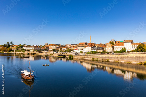 France, Nouvelle-Aquitaine, Bergerac, Boat sailing alongDordogne River with old town buildings in background