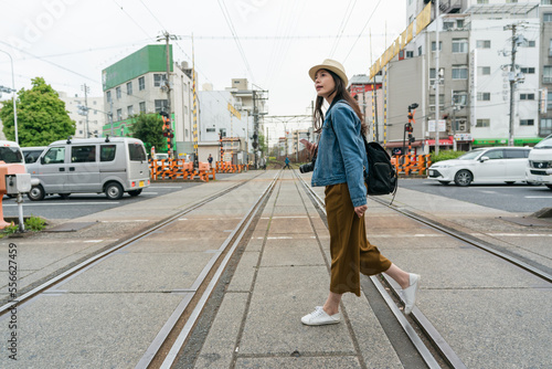 full length with side view asian female traveler passing by railroad crossing in downtown Osaka, japan in spring at daytime