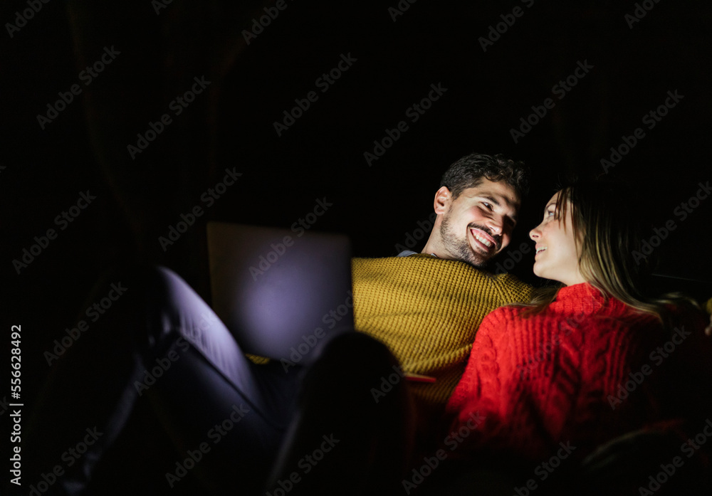 Happy couple using laptop at night smiling at each other