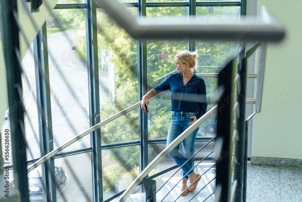 Thoughtful businesswoman standing on staircase at office Thoughtful businesswoman standing on staircase at office
