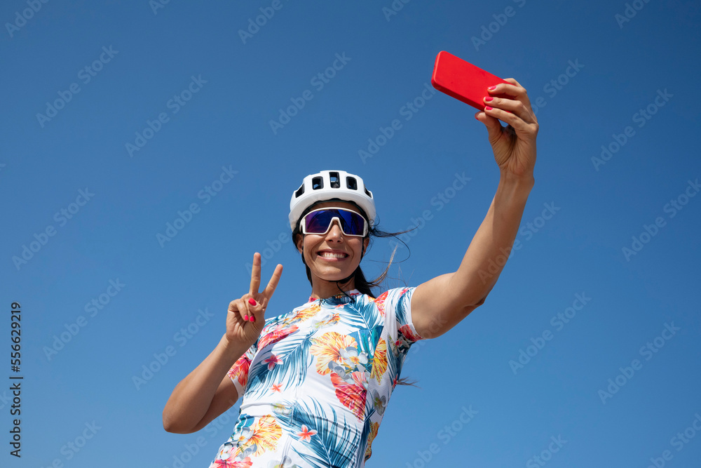 Happy cyclist showing peace gesture and taking selfie through smart phone Happy cyclist showing peace gesture and taking selfie through smart phone