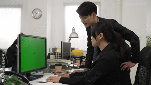 asian colleagues wearing suit pointing at computer with green screen while working together discussing statistics in modern office at investing company