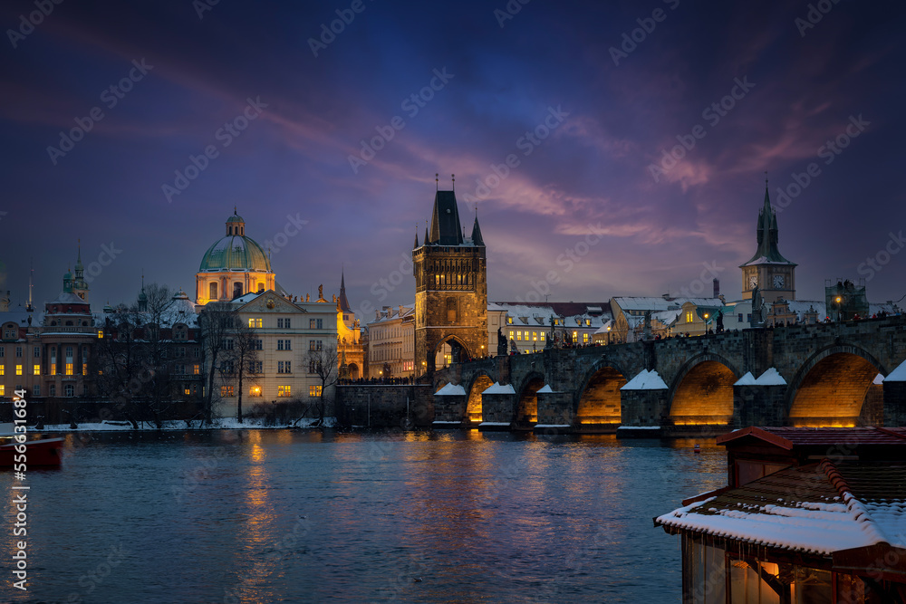 Fototapeta premium Beautiful winter evening view of the illuminated skyline of Prague with Charles Bridge and the snow covered old town roofs, Czezch Republic 