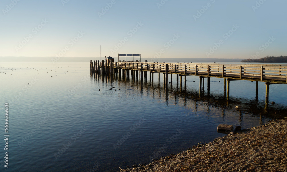 a long wooden pier in Herrsching on calm Lake Ammersee in Bavaria on a clear January evening (Herrsching, Bavaria, Germany)