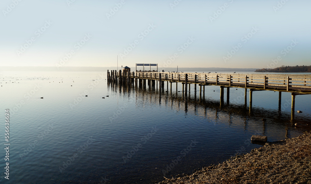 a long wooden pier in Herrsching on calm lake Ammersee in Bavaria on a clear serene January evening (Herrsching, Bavaria, Germany)	