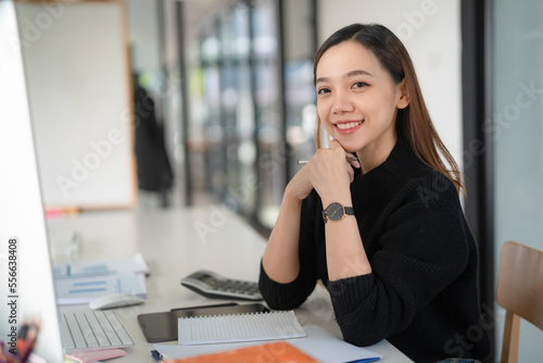 A pretty businesswoman smiles at the camera while sitting at her desk in front of the computer.