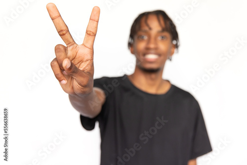 Close-up of peace sign made by positive young man. Male African American model with brown eyes and afro braids in black T-shirt smiling and showing victory sign. Confidence, self-assurance concept