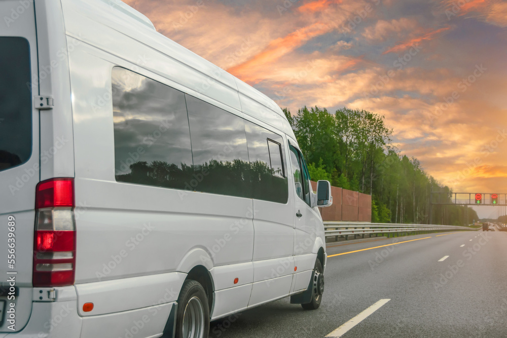 White modern passenger charter van with a small delivery moves fast on the highway to the urban suburbs. Business distribution and logistics express service. Mini bus rides along the highway.