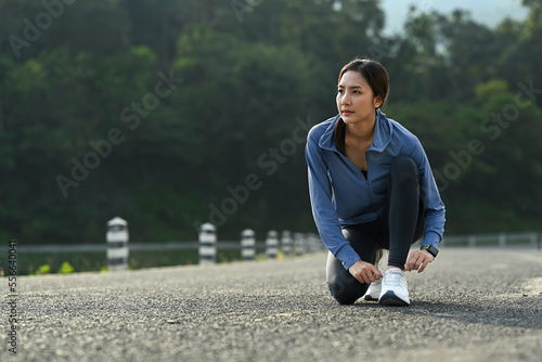 Photo of sportswoman tying shoelace before running outdoors. Fitness, sport and healthy lifestyle concept