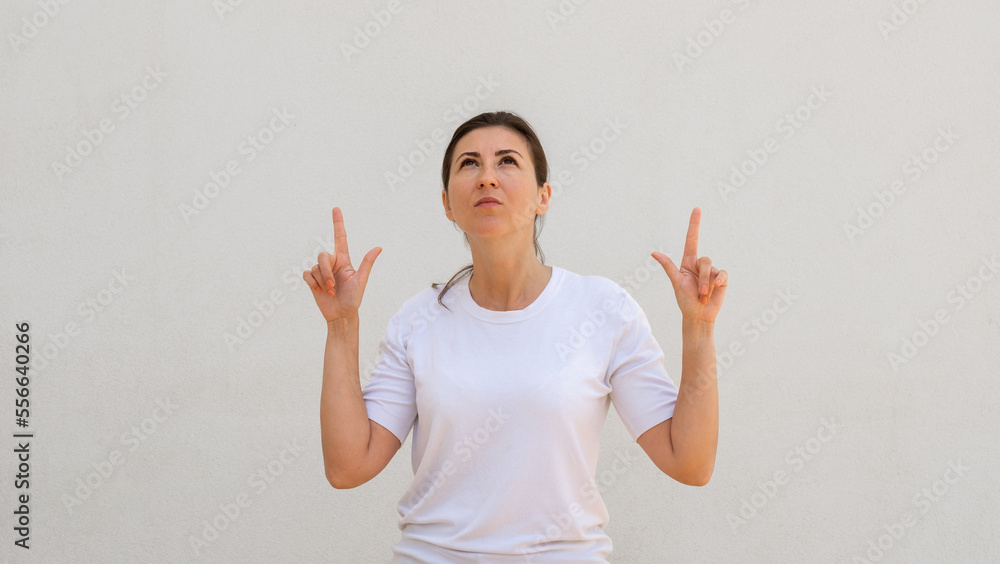 Portrait of concentrated young woman pointing upwards over white background. Caucasian woman wearing white T-shirt showing something. Advertising concept Portrait of concentrated young woman pointing upwards over white background. Caucasian woman wearing white T-shirt showing something. Advertising concept