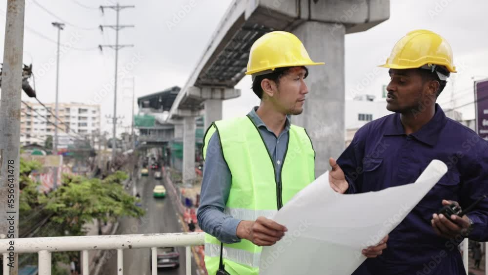 Structural engineers and construction workers are holding blueprints inspecting structure. sky train track construction in city. Blue collar wears a safety hardhat while working on construction site. Structural engineers and construction workers are holding blueprints inspecting structure. sky train track construction in city. Blue collar wears a safety hardhat while working on construction site.