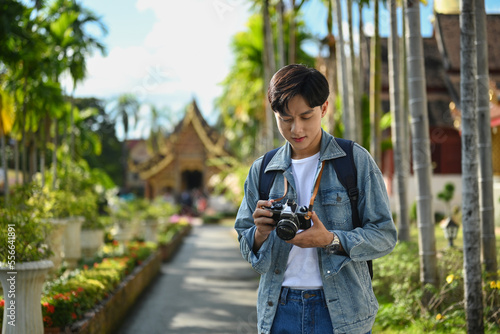 Young male tourist with backpack and digital camera standing in buddhist temple. Blogger, vacation and journey concept
