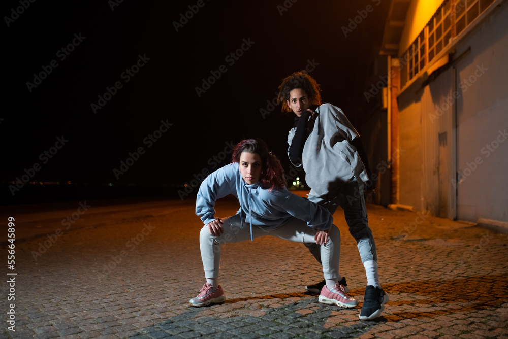 Cool male and female dancers at night. Man and woman in modern clothes looking at camera and standing in dancing poses. Dancing, hobby concept Cool male and female dancers at night. Man and woman in modern clothes looking at camera and standing in dancing poses. Dancing, hobby concept