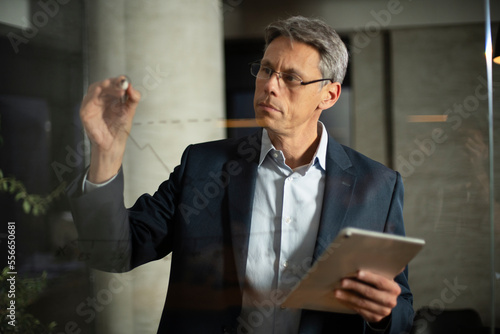 Portrait of successful businessman in office. Man writing on the glass board in office