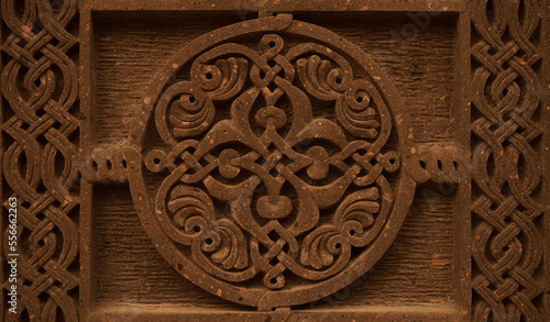 Carved round ornament with intertwining strips forming a pattern placed in a round frame on a red volcanic stone. Traditional tufa stone carving ornament on a wall of Armenian Orthodox Church. photo