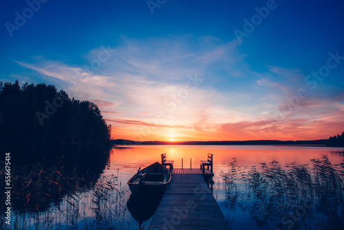 Sunset on a lake. Wooden pier with fishing boat at sunset in Finland © nblxer