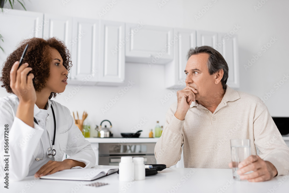 African american doctor talking to middle aged man with diabetes near notebook and pills at home African american doctor talking to middle aged man with diabetes near notebook and pills at home