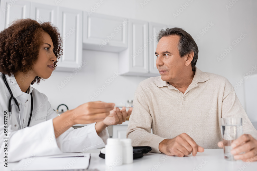 Fototapeta premium curly african american doctor showing lancet pen to middle aged patient with diabetes